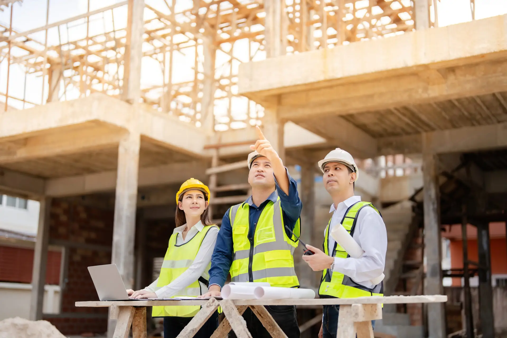 Three Asian engineers in high-vis jackets on a construction site for an energy-efficient factory.